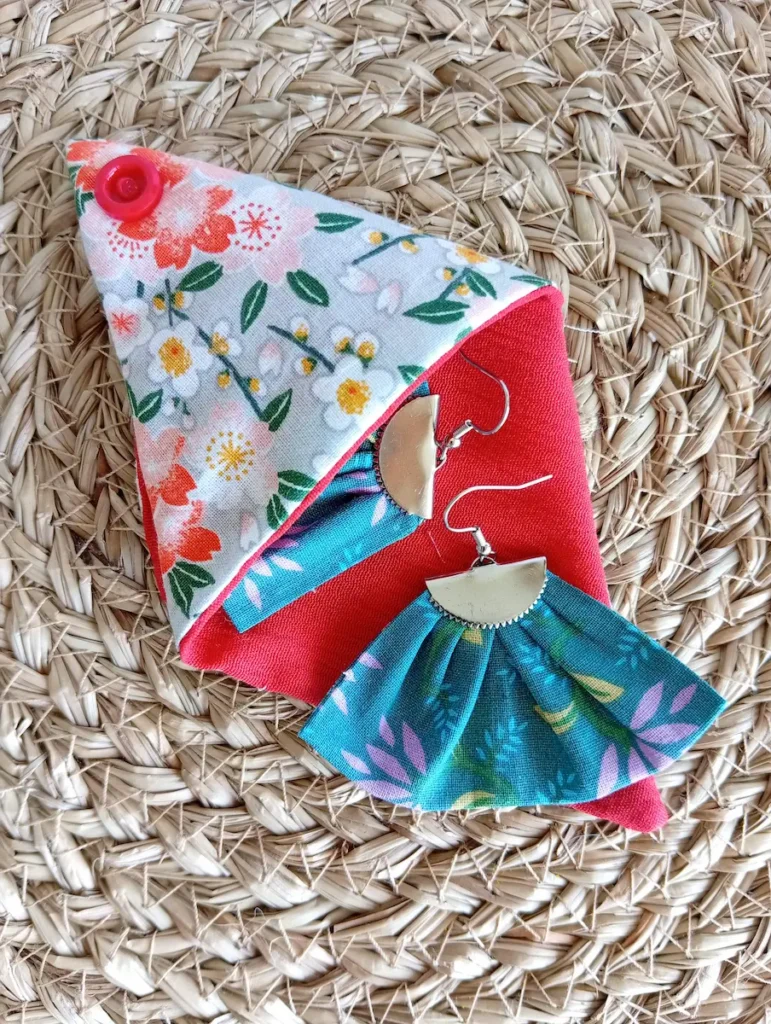 pochette origami fleurs rouge contenant des boucles d'oreille éventail motif fleurs mauve sur fond bleu-vert