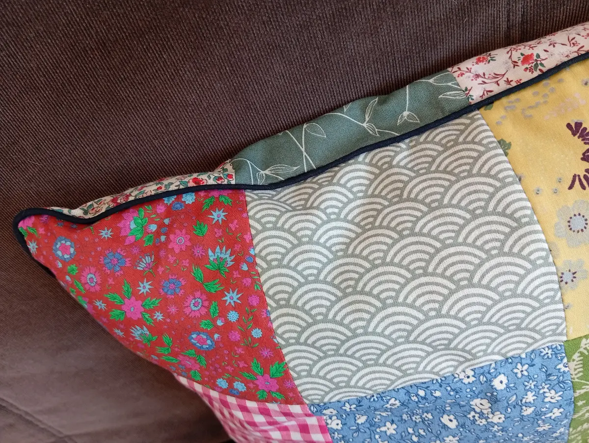 détail du coussin en patchwork de fleurs issu de l'upcycling où on voit bien la finition au liseret bleu marine