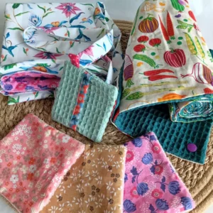 kit zéro déchet au quotidien par Cousu Mel Le Havre : un sac de course réversible à fleurs roses, un rouleau d'essuie-tout motif fruits et légumes, 3 lingettes lavables en bambou motifs petites fleurs roses et ocre et une pochette sauve-savon bleu clair avec bord à fleurs