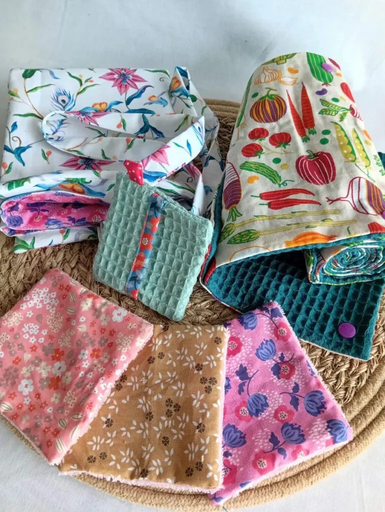 kit zéro déchet au quotidien par Cousu Mel Le Havre : un sac de course réversible à fleurs roses, un rouleau d'essuie-tout motif fruits et légumes, 3 lingettes lavables en bambou motifs petites fleurs roses et ocre et une pochette sauve-savon bleu clair avec bord à fleurs