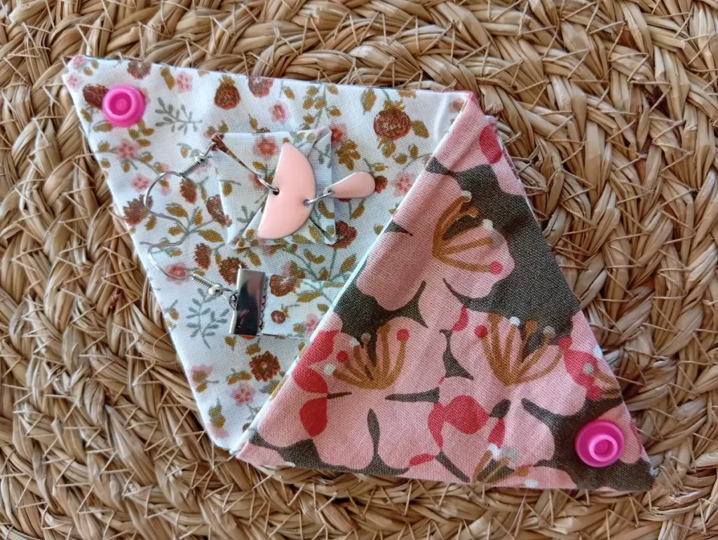 Pochette origami emballage cadeau contenant les boucles d'oreilles asymétriques artisanales aux mêmes motifs à petites fleurs marrons, pêches et vertes sur fond blanc