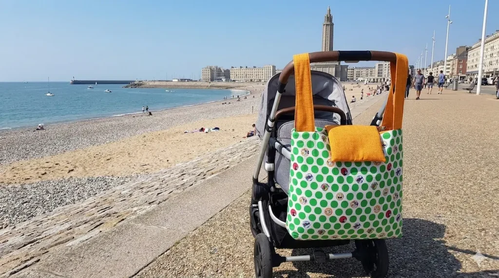 sac à langer nomade avec accessoires indispensable en tissu fait main Cousu Mel motif pois verts accrochée à une poussette sur la digue du Havre face à la mer.