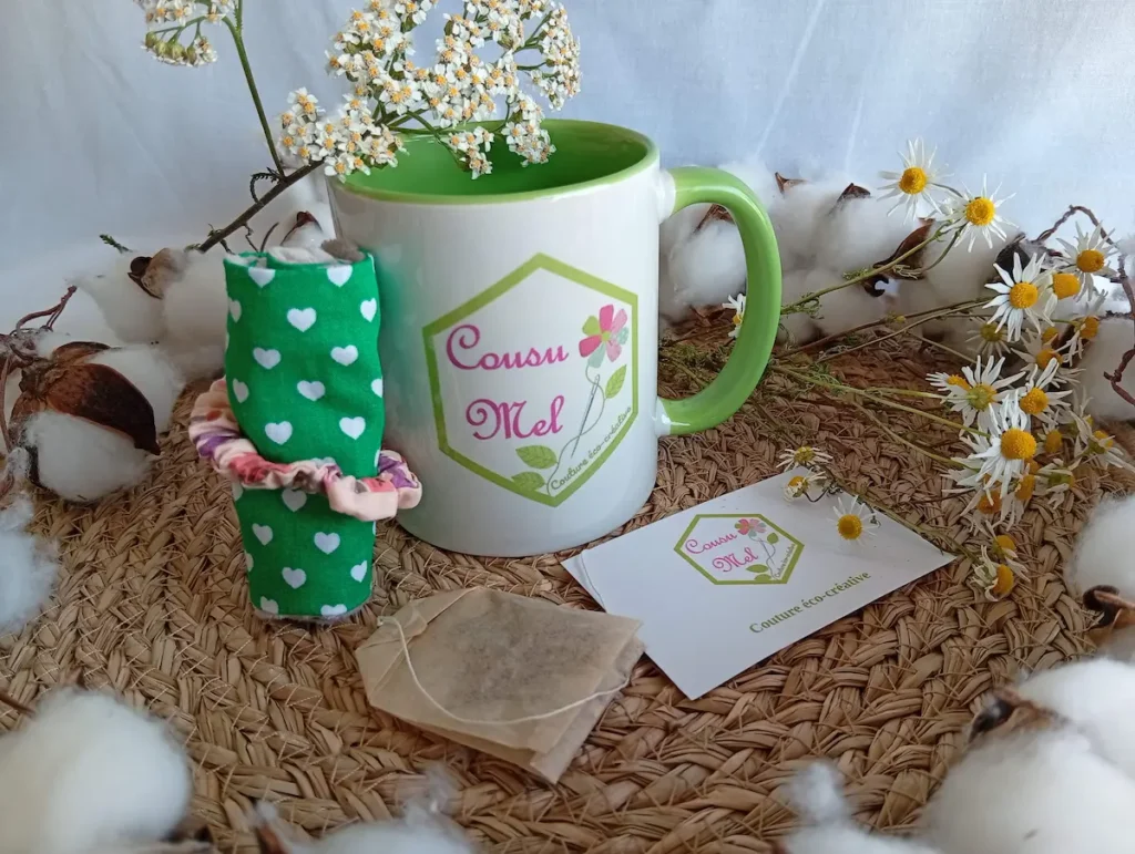 Coffret pause détente Cousu Mel comprenant un mug logo, une housse de tasse verte à motifs cœurs et un sachet d'infusion.